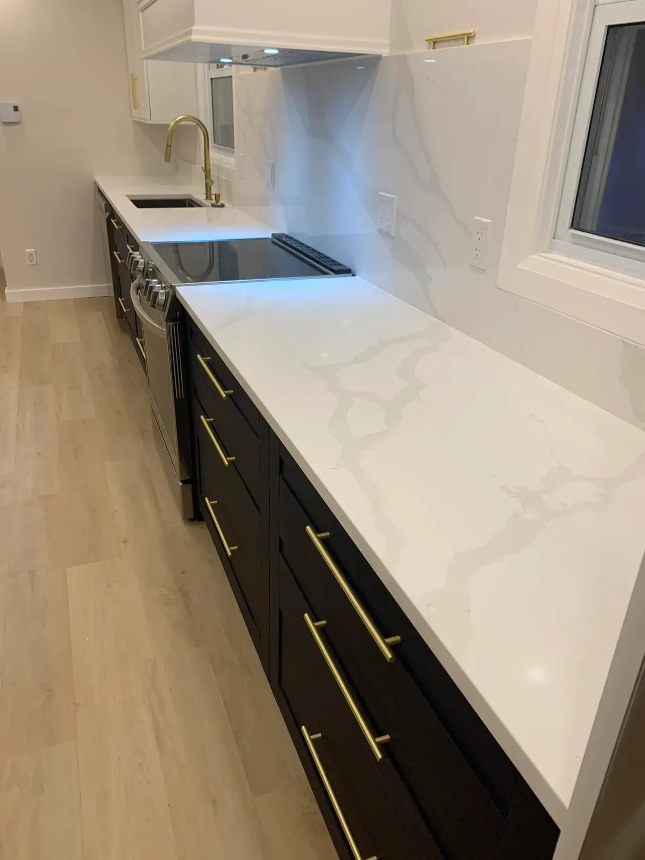 Countertop and full-height slab backsplash over black cabinets, a Prime Stone and Tile kitchen shown by Blueprint Cabinets